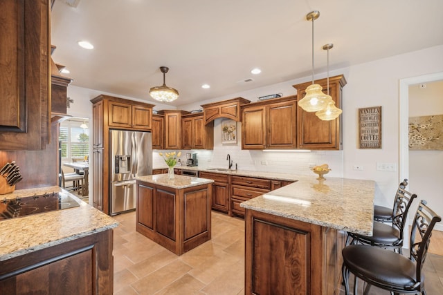 kitchen with light stone countertops, a center island, stainless steel fridge, and decorative light fixtures