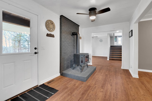 entrance foyer featuring hardwood / wood-style flooring, ceiling fan, ornamental molding, and a wood stove