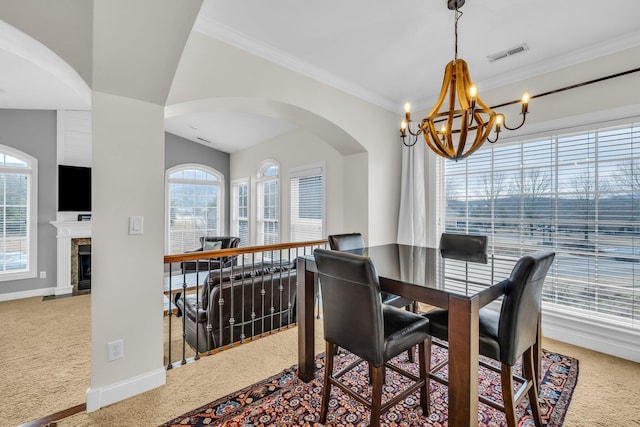 carpeted dining room featuring a tile fireplace, a healthy amount of sunlight, crown molding, and an inviting chandelier