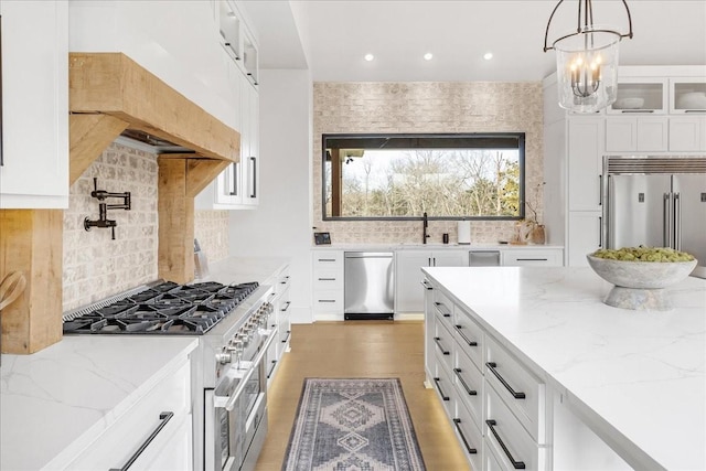 kitchen featuring high end appliances, pendant lighting, light stone countertops, and white cabinets