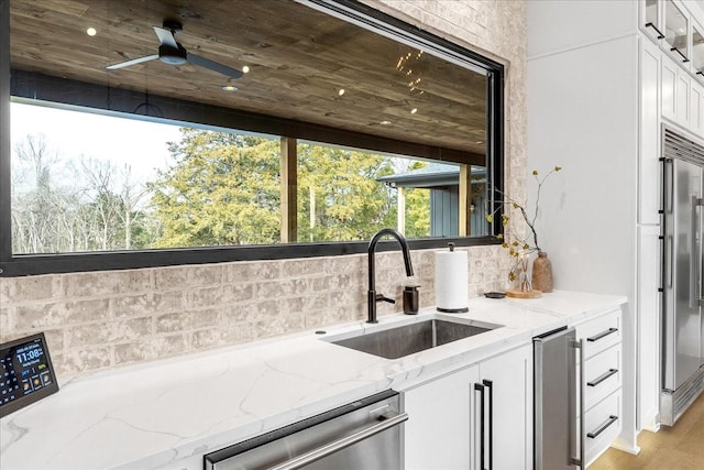 kitchen with appliances with stainless steel finishes, sink, white cabinets, decorative backsplash, and light stone countertops