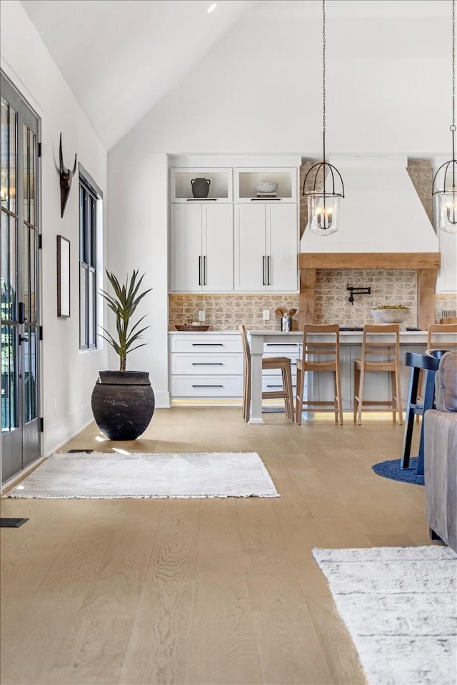 kitchen with backsplash, high vaulted ceiling, a notable chandelier, white cabinets, and decorative light fixtures