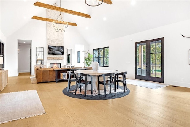 dining space with french doors, high vaulted ceiling, light wood-type flooring, a large fireplace, and beam ceiling