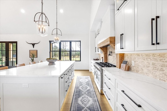 kitchen with hanging light fixtures, stainless steel stove, custom exhaust hood, and white cabinets