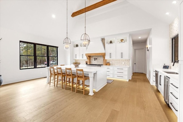 kitchen with sink, a breakfast bar, a center island, custom range hood, and white cabinets