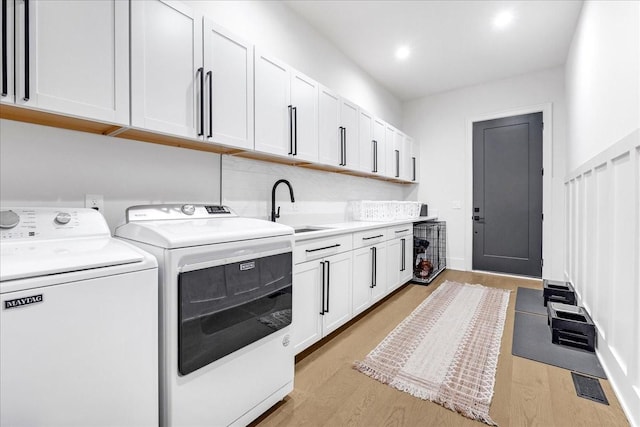 laundry area featuring cabinets, washing machine and clothes dryer, sink, and light wood-type flooring