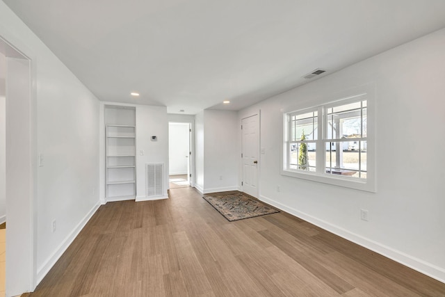 unfurnished living room featuring built in features and light wood-type flooring