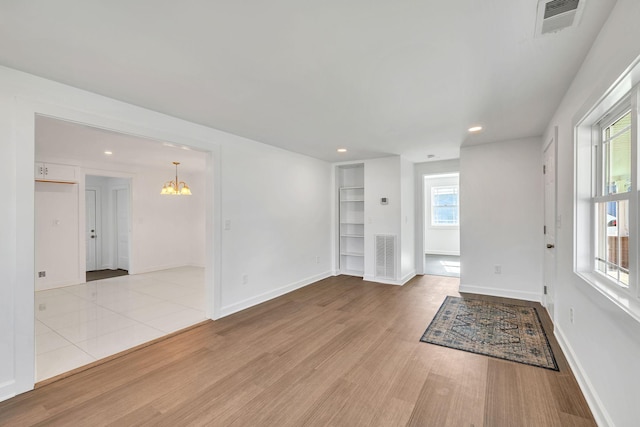 unfurnished living room featuring an inviting chandelier and light hardwood / wood-style flooring