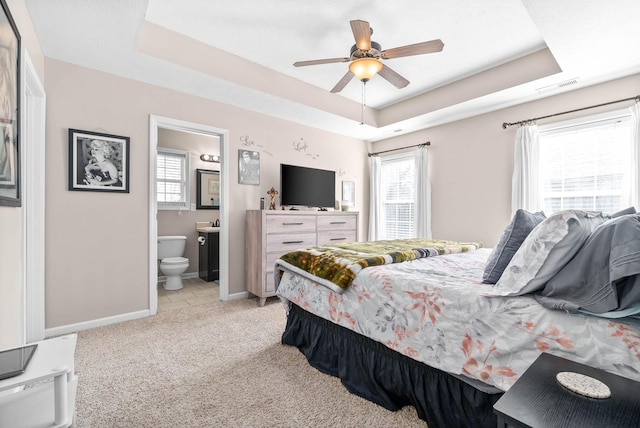 carpeted bedroom with ceiling fan, ensuite bath, a raised ceiling, and multiple windows