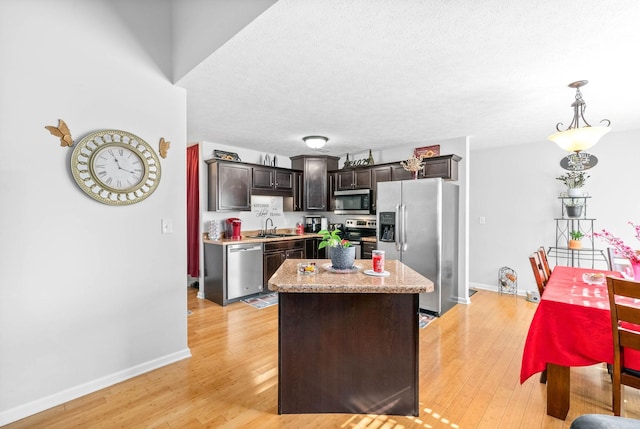 kitchen featuring sink, stainless steel appliances, dark brown cabinetry, a kitchen island, and decorative light fixtures