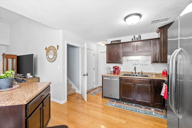 kitchen with dark brown cabinetry, sink, a textured ceiling, light wood-type flooring, and stainless steel appliances