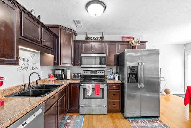 kitchen with sink, a textured ceiling, appliances with stainless steel finishes, light stone countertops, and light hardwood / wood-style floors