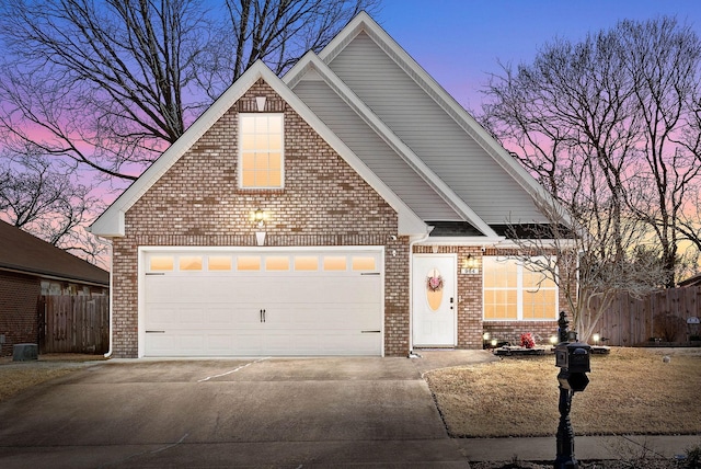 traditional-style house with a garage, brick siding, driveway, and fence