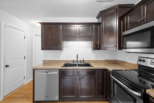 kitchen with stainless steel appliances, dark brown cabinets, light countertops, light wood-type flooring, and a sink