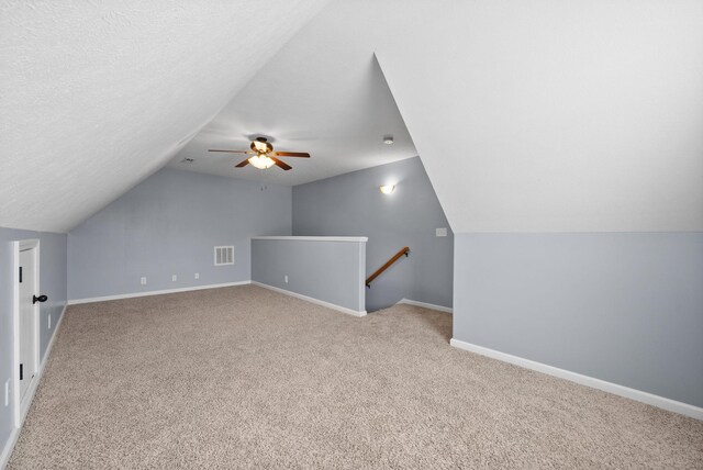 bonus room featuring a textured ceiling, lofted ceiling, visible vents, baseboards, and carpet