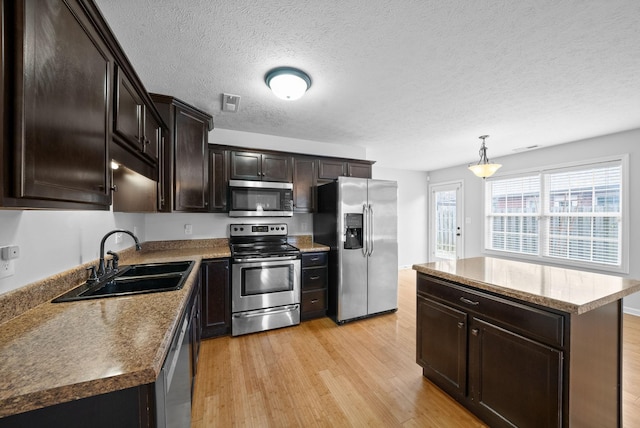 kitchen with light wood-style flooring, a sink, appliances with stainless steel finishes, a center island, and decorative light fixtures