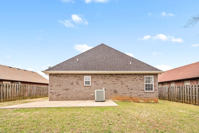 rear view of house featuring brick siding, roof with shingles, a lawn, and a patio