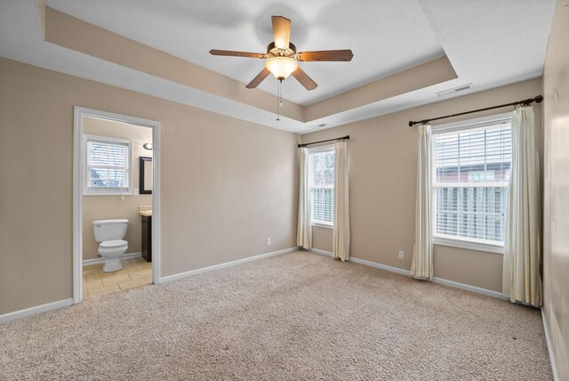 unfurnished bedroom featuring a tray ceiling, carpet flooring, visible vents, and baseboards