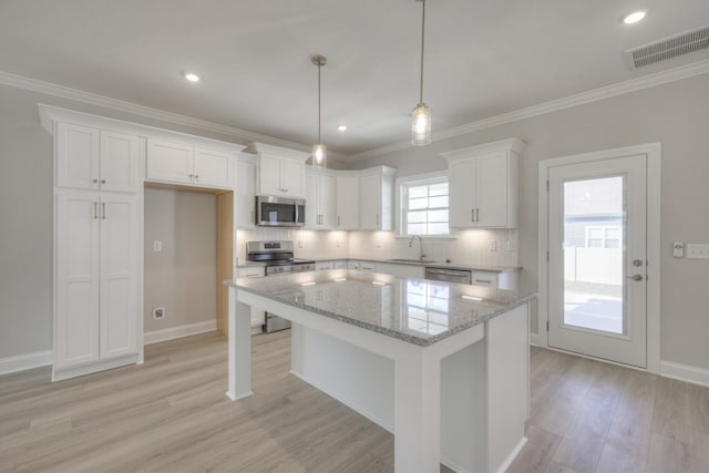 kitchen featuring pendant lighting, appliances with stainless steel finishes, white cabinetry, light stone counters, and a kitchen island