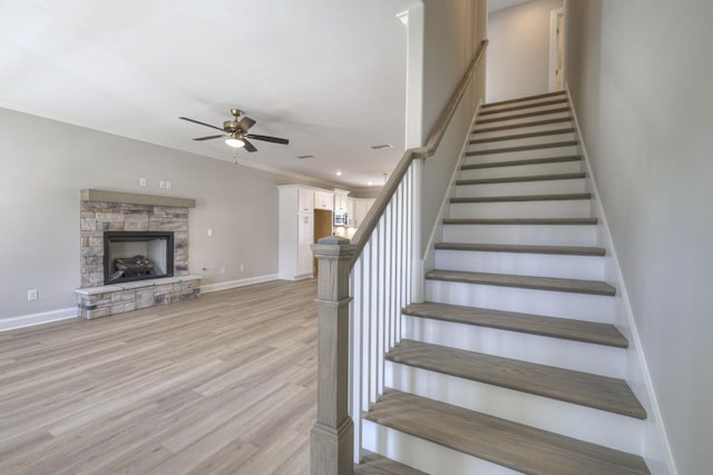 staircase with hardwood / wood-style floors, a fireplace, ornamental molding, and ceiling fan