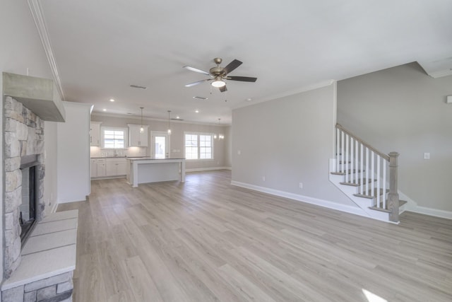 unfurnished living room with crown molding, a stone fireplace, ceiling fan, and light hardwood / wood-style floors