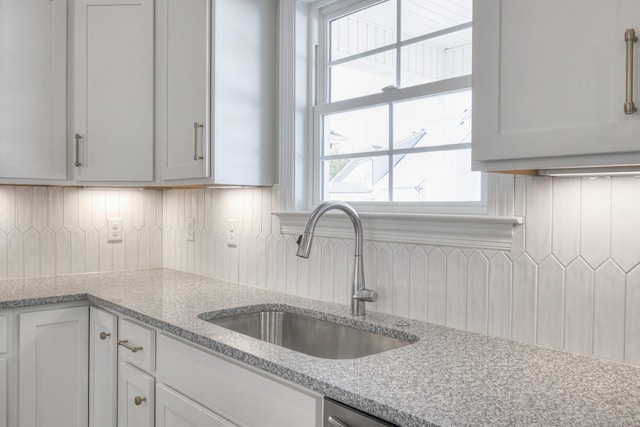 kitchen with tasteful backsplash, white cabinetry, light stone countertops, and sink