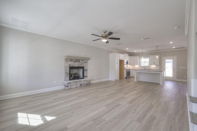 unfurnished living room featuring ornamental molding, ceiling fan, a fireplace, and light wood-type flooring