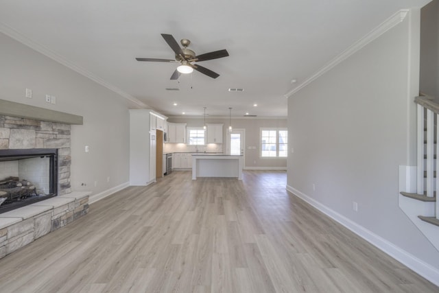 unfurnished living room featuring crown molding, a stone fireplace, ceiling fan, and light wood-type flooring