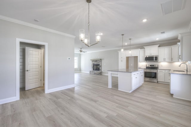 kitchen with a stone fireplace, hanging light fixtures, appliances with stainless steel finishes, a kitchen island, and white cabinets