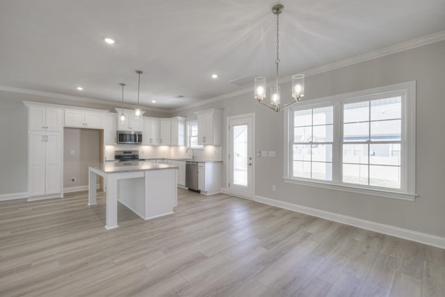 kitchen with white cabinets, hanging light fixtures, ornamental molding, a center island, and stainless steel appliances