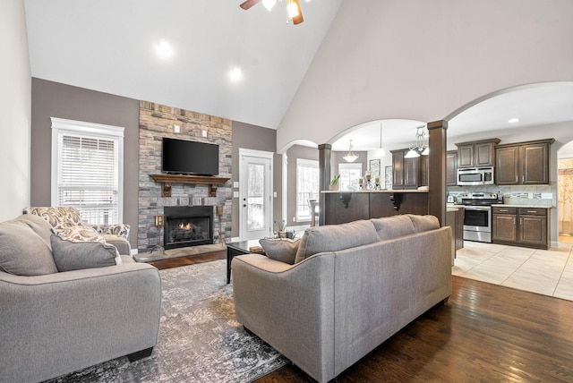 living room with wood-type flooring, a stone fireplace, a wealth of natural light, and ceiling fan