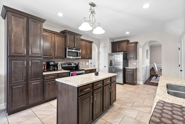 kitchen with a center island, dark brown cabinets, hanging light fixtures, appliances with stainless steel finishes, and backsplash