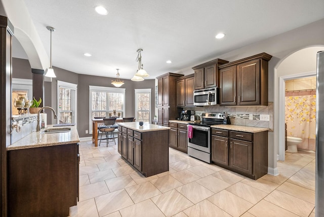 kitchen with a kitchen island, appliances with stainless steel finishes, decorative light fixtures, sink, and dark brown cabinets