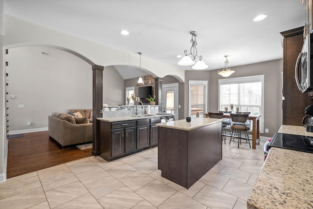 kitchen featuring light stone counters, decorative light fixtures, a center island, and sink