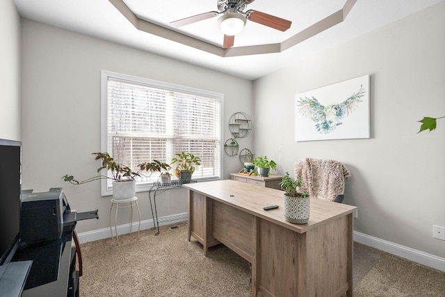 carpeted office featuring a raised ceiling and ceiling fan