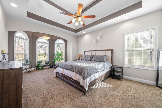 carpeted bedroom with ceiling fan and a raised ceiling