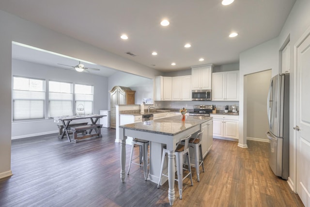 kitchen featuring appliances with stainless steel finishes, white cabinets, a kitchen bar, a center island, and light stone counters