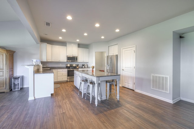 kitchen with dark wood-type flooring, a kitchen bar, appliances with stainless steel finishes, a kitchen island, and white cabinets