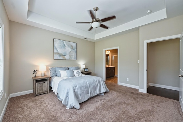 carpeted bedroom with connected bathroom, a tray ceiling, and ceiling fan