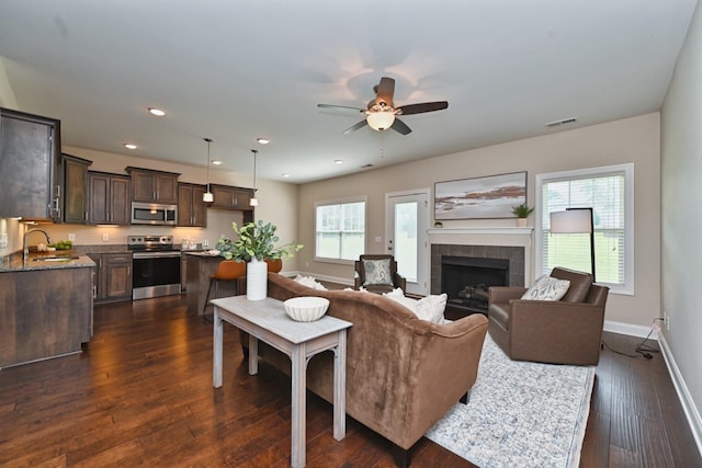 living room featuring dark hardwood / wood-style flooring, sink, a tiled fireplace, and ceiling fan