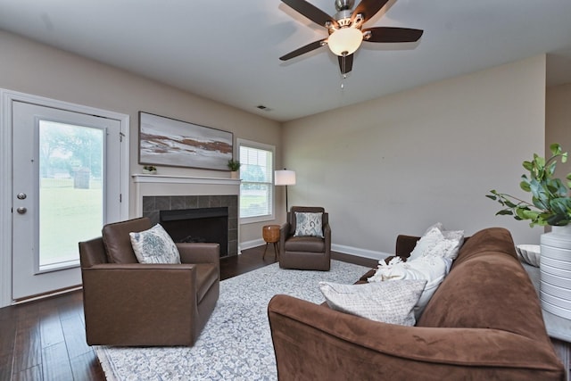 living room featuring dark wood-type flooring, ceiling fan, and a tile fireplace