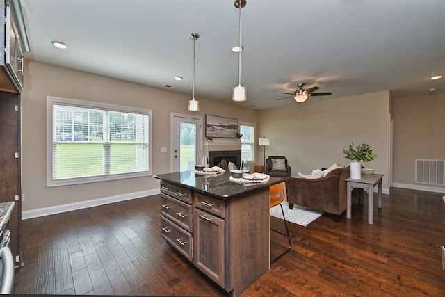 kitchen featuring dark hardwood / wood-style floors, pendant lighting, a breakfast bar, dark stone counters, and a center island