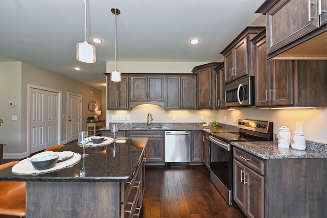 kitchen with dark brown cabinetry, appliances with stainless steel finishes, a kitchen island, and dark stone countertops