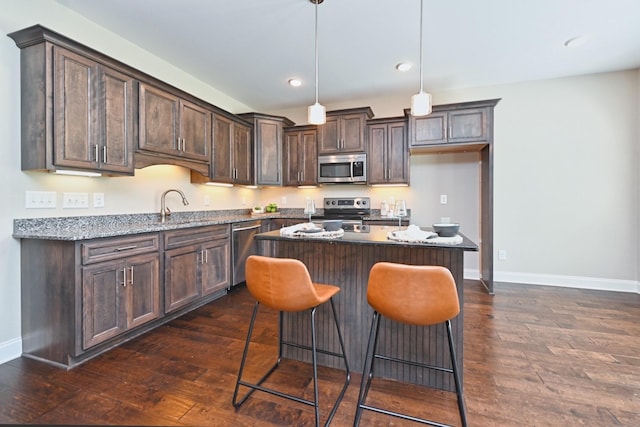 kitchen with pendant lighting, appliances with stainless steel finishes, dark hardwood / wood-style floors, a center island, and light stone counters