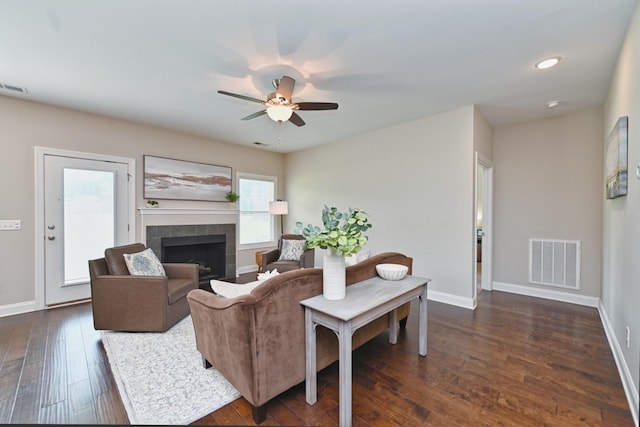 living room with a tiled fireplace, dark hardwood / wood-style floors, and ceiling fan