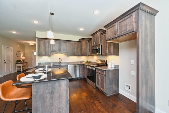 kitchen featuring sink, dark stone countertops, hanging light fixtures, stainless steel appliances, and a center island