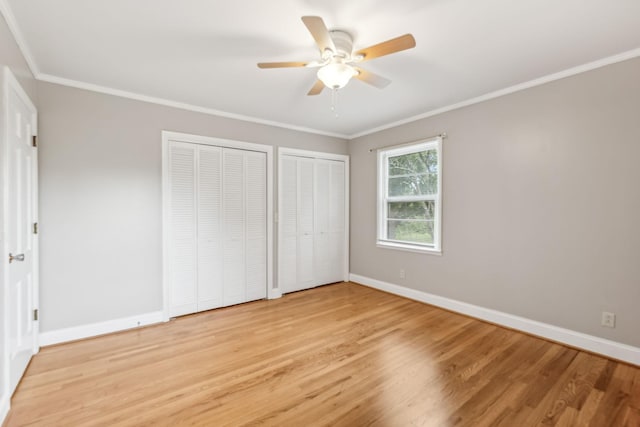 unfurnished bedroom with two closets, ornamental molding, light hardwood / wood-style floors, and ceiling fan