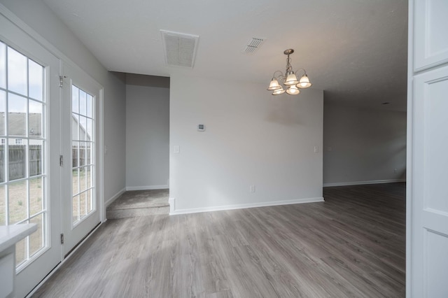 empty room with a healthy amount of sunlight, a chandelier, and light hardwood / wood-style flooring