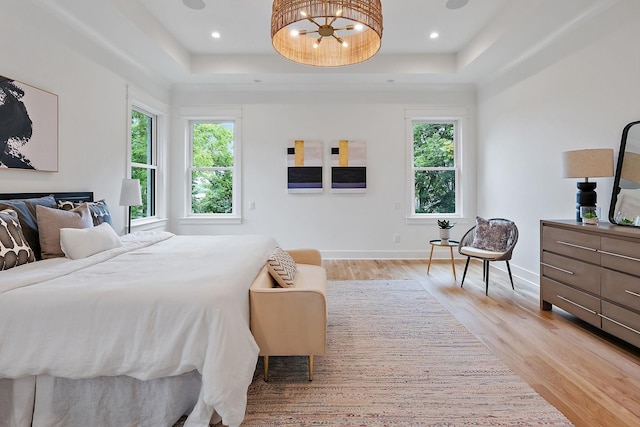 bedroom featuring multiple windows, a notable chandelier, light hardwood / wood-style floors, and a tray ceiling