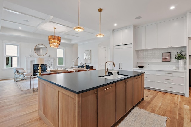 kitchen with coffered ceiling, a kitchen island with sink, sink, and white cabinets